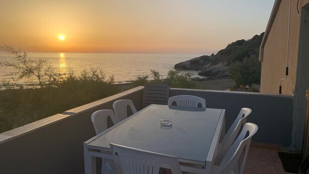 Una terraza con mesa y sillas con vista a la puesta de sol sobre el mar.