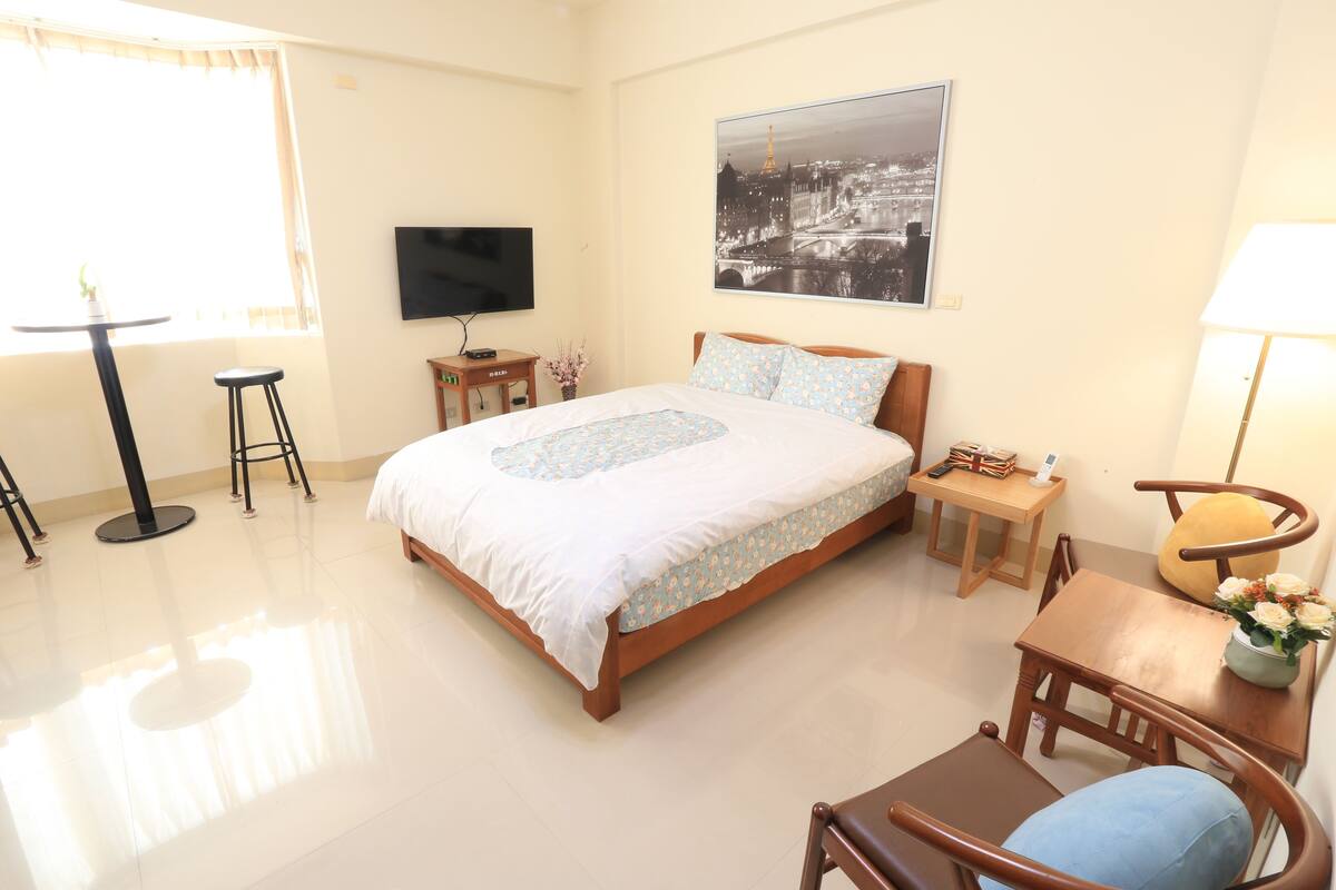 A hotel room with a bed, a TV, a table with chairs, and a window with curtains.