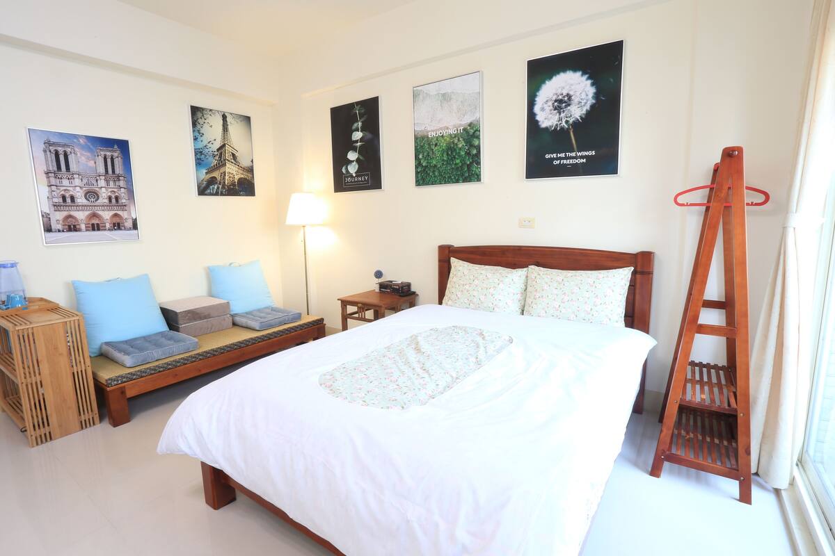 A neatly arranged bedroom with a bed, bedside tables, a wooden ladder, and wall art including a dandelion and Eiffel Tower.