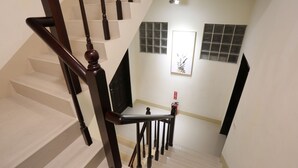 A staircase with wooden balusters and a handrail, leading to a landing with a framed artwork and a fire extinguisher. - Downshifted House (Miaoli)