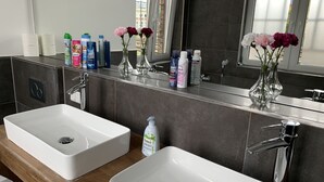 Ein modernes Badezimmer mit zwei weißen Waschbecken, einem Spiegel und verschiedenen Pflegeprodukten auf der Ablagefläche.