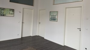 Ein Flur mit drei weißen Türen, jede mit einer Nummer gekennzeichnet. An den Wänden hängen zwei gerahmte Kunstwerke, eines zeigt ein Gebäude und das andere eine Kutsche. Der Boden ist dunkles Holz und die Decke hat einen schwarzen Balken.