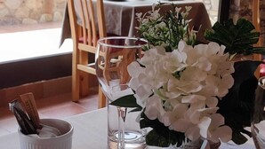 A dining table set with white plates, cutlery, and a glass. There is a vase with white flowers and a candle holder with a candle. - Hotel Ransol (Ransol)