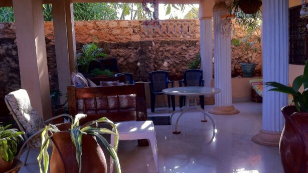 An outdoor patio area with a stone wall, seating, and potted plants. - Sadiana Apartments (Mtwapa)