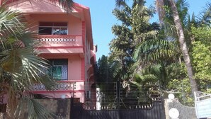 A pink building with a gated entrance, surrounded by palm trees and other greenery. - Sadiana Apartments (Mtwapa)