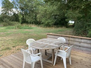 Une terrasse extérieure en bois avec une table ronde et quatre chaises en plastique blanc.