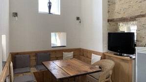 A modern kitchen with a wooden table and bench seating, a television, and a small window. - The Bahutière Annex and the Pineau (La chapelle sur oudon)