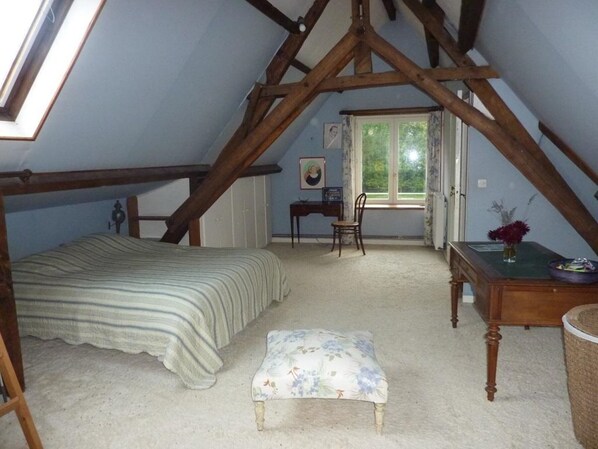 Une chambre avec un plafond en pente, un lit, une chaise, une petite table et une fenêtre.