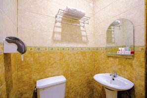A bathroom with yellow tiles, a toilet, a sink, a towel rack, and a mirror. - OYO 1770 Hotel Mawar Saron 2 (Depok)