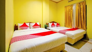 Habitación de hotel con dos camas, cada una con ropa de cama blanca y detalles en rojo, paredes amarillas y una ventana con cortinas amarillas.
