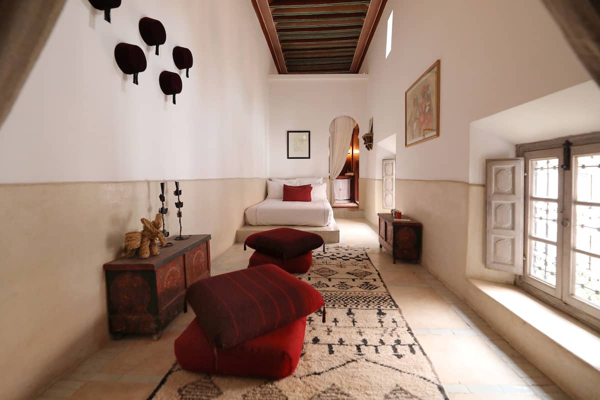 A bedroom with a bed, a red sofa, a patterned rug, and a window with bars.