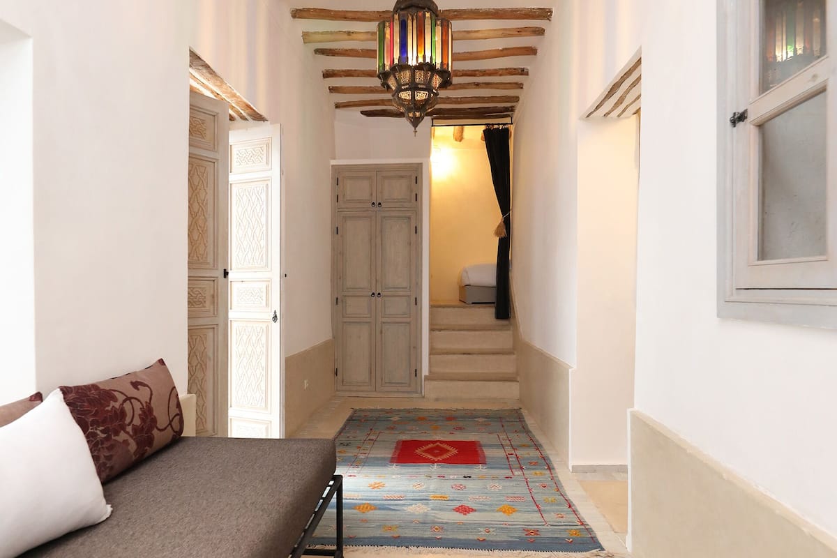 A narrow hallway with a bed, a glass table with a candle, and a wooden ceiling.
