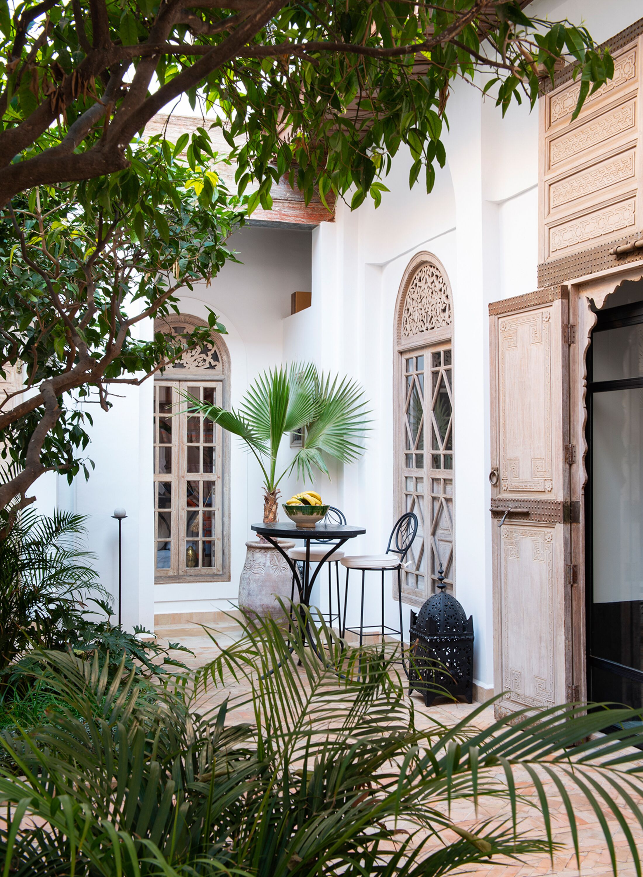 A courtyard with a table, chairs, a potted plant, and a decorative lantern.