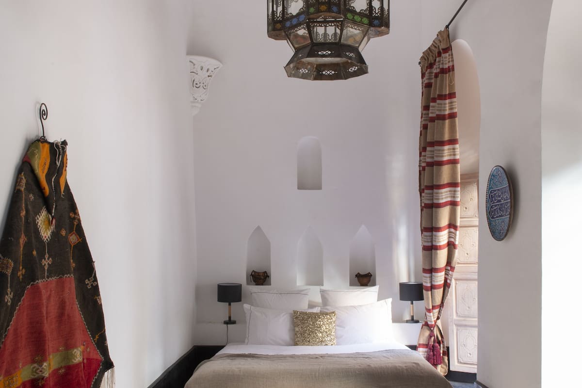 A bedroom with a bed, a hanging lantern, and a view of the outside.