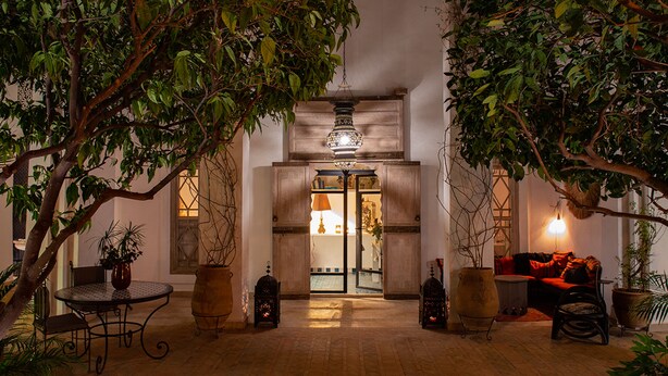 Un patio interior con una mesa de madera, sillas, plantas en macetas y un sofá.