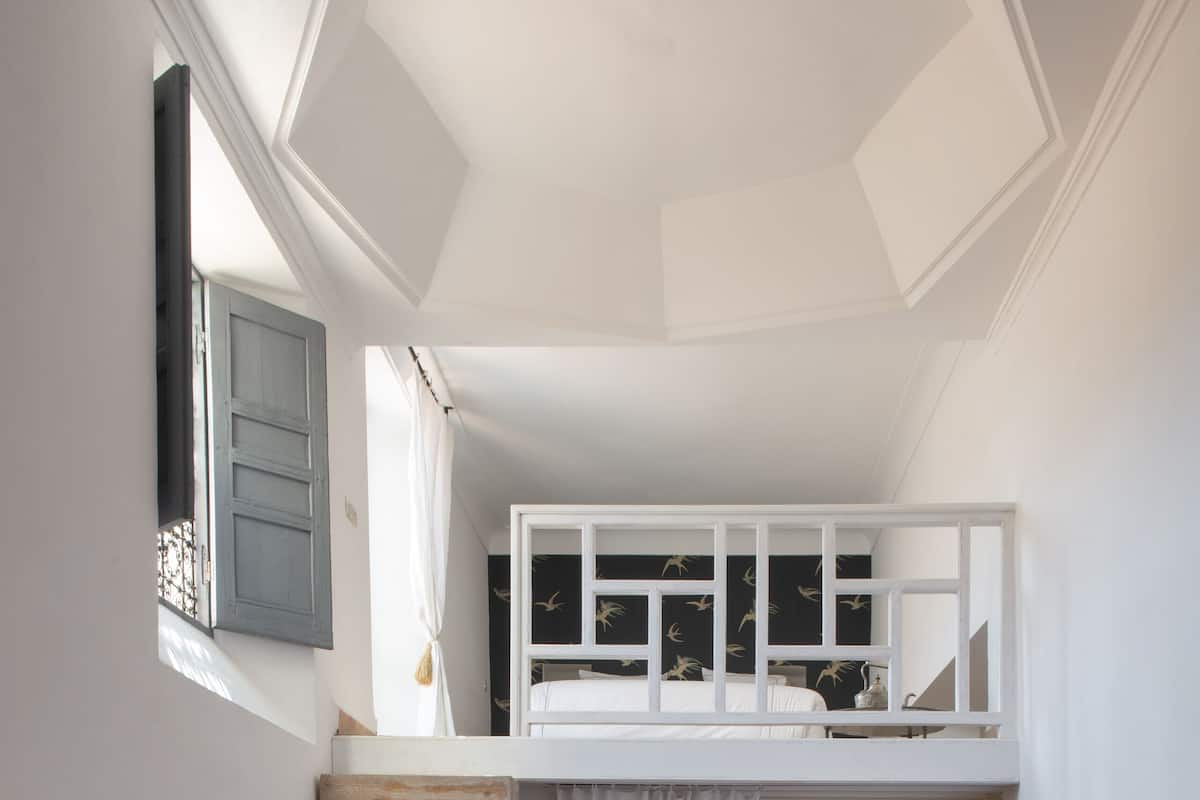 A bedroom with a wooden staircase, a red carpet, a bed with white bedding, and a small wooden bench.