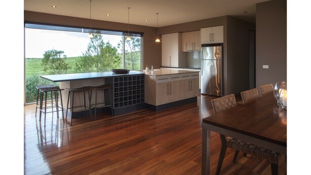A modern kitchen with a large island, bar stools, and a dining area with a table and chairs. - THE Lake House - Surf Side (Inverloch)