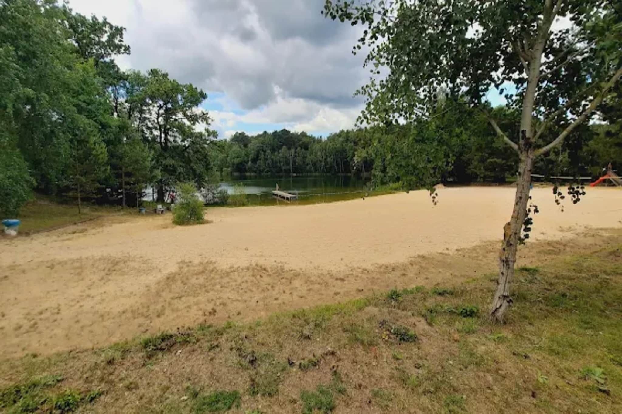 A sandy beach area with a small dock and trees in the background.