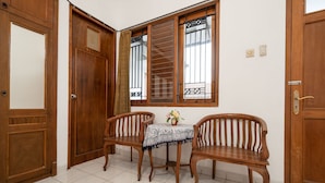 A room with two wooden chairs, a small table with a patterned tablecloth, and a window with bars.