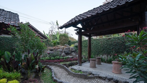 A traditional Japanese-style garden with a stone pathway, a wooden gazebo, and various plants.