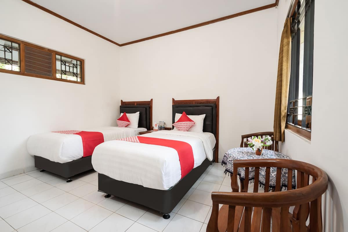 Habitación de hotel con dos camas, una mesita con un florero y una silla.