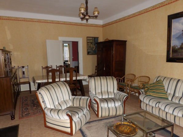 A living room with striped armchairs, a sofa, a glass coffee table, and a dining area with a table and chairs.
