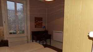 Ett sovrum med en säng, ett skrivbord, en stol, ett element och ett fönster med utsikt över omgivningen.