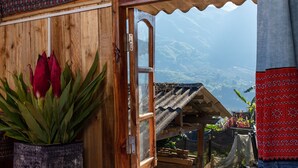 A room with a wooden door, a blue patterned bedspread, and a red and black patterned tapestry. - Zizi Homestay and Trekking - Hostel (Ta Van)