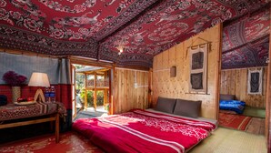A traditional room with a wooden interior, a large bed with a red and white bedspread, a wooden desk with a lamp, and a view of the outdoors. - Zizi Homestay and Trekking - Hostel (Ta Van)