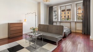 Una sala de estar moderna con sofá, una mesita, una lámpara de pie y vistas a edificios a través de amplios ventanales.