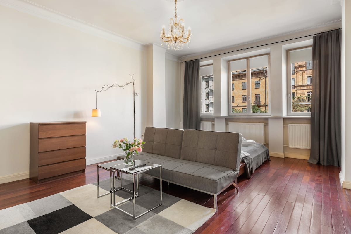 Ein modernes Wohnzimmer mit einer Couch, einem kleinen Tisch, einer Stehlampe und Blick auf Gebäude durch große Fenster.