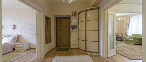 Un pasillo de hotel con piso de madera, alfombra blanca, una puerta con un letrero y una habitación con cama y mesita de noche.