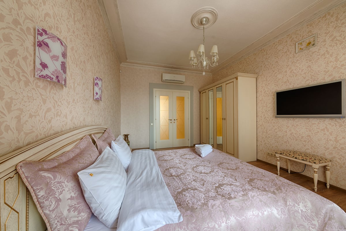 Ein Schlafzimmer mit einem großen Bett, einer Chandelüster, einem Fernseher und einem Kleiderschrank.
