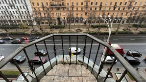 Vista desde un balcón con vista a una calle concurrida, autos, una acera para peatones y edificios históricos al fondo.