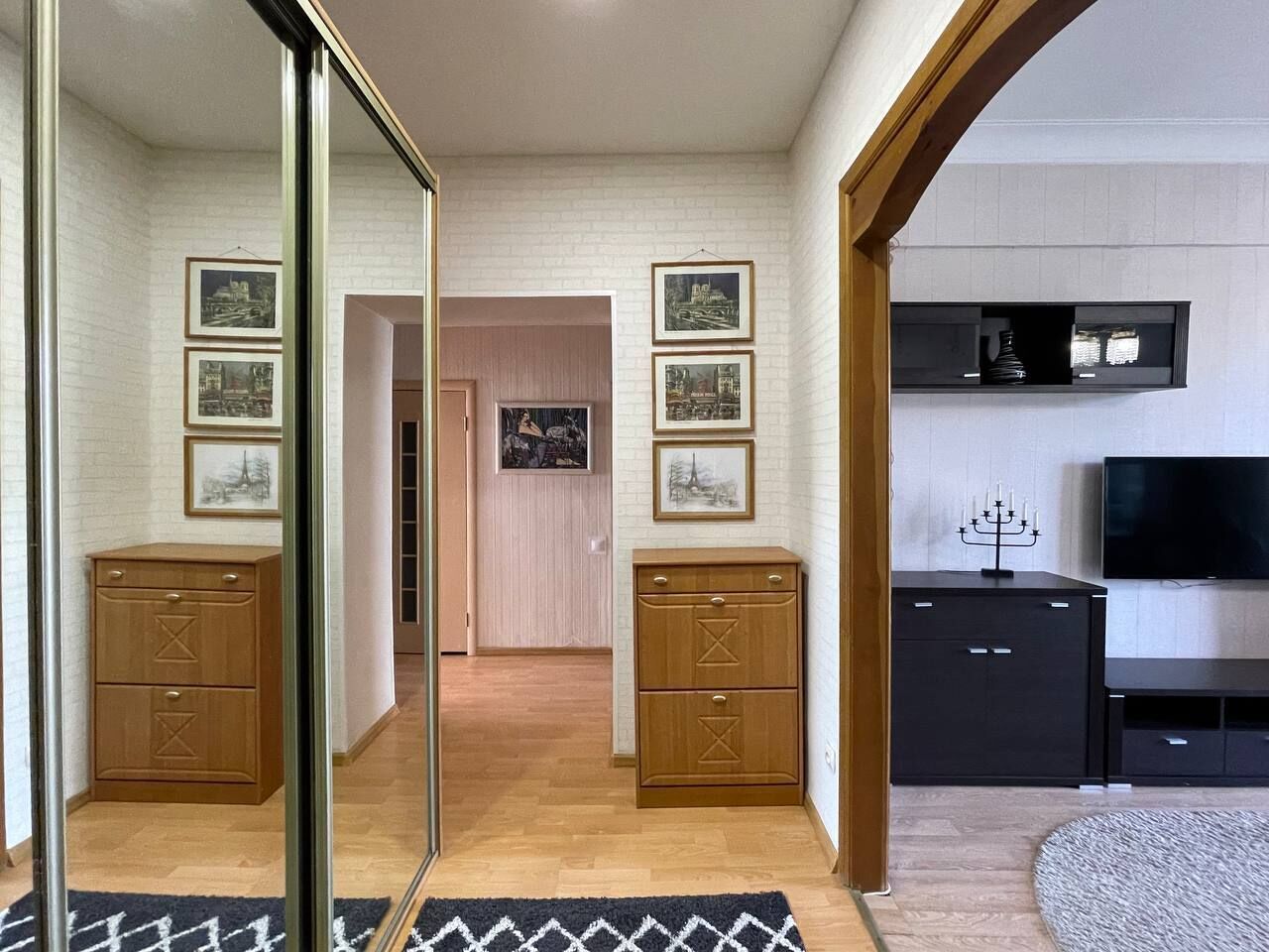A modern living room with a wooden cabinet, a black entertainment unit, and framed pictures on the wall.