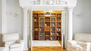 Una habitación amplia con una gran estantería de madera, un sillón blanco y una araña.