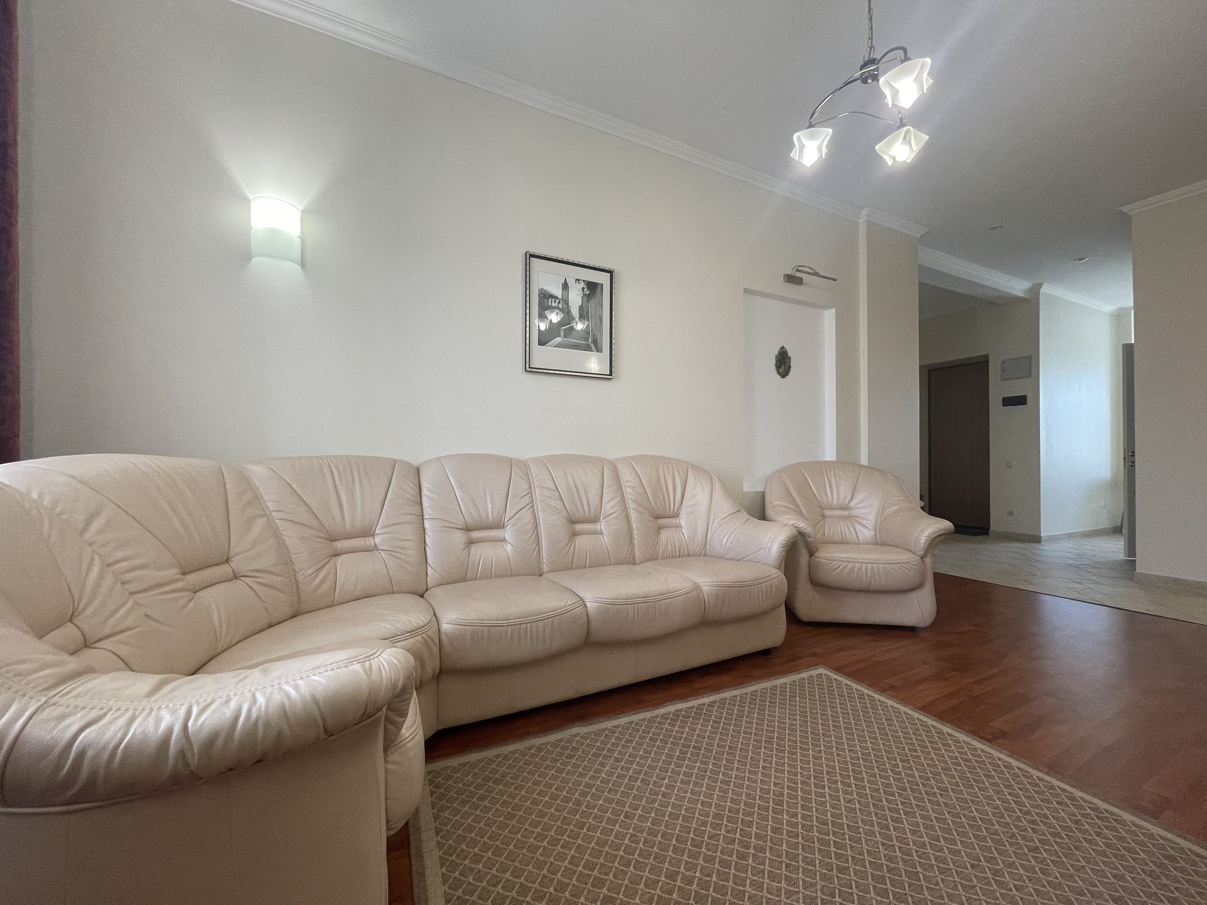 A living room with a beige leather sectional sofa, a matching armchair, a patterned rug, and a framed picture on the wall.