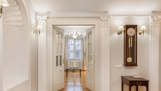 Un pasillo con puertas blancas, piso de madera y un espejo grande con un reloj.