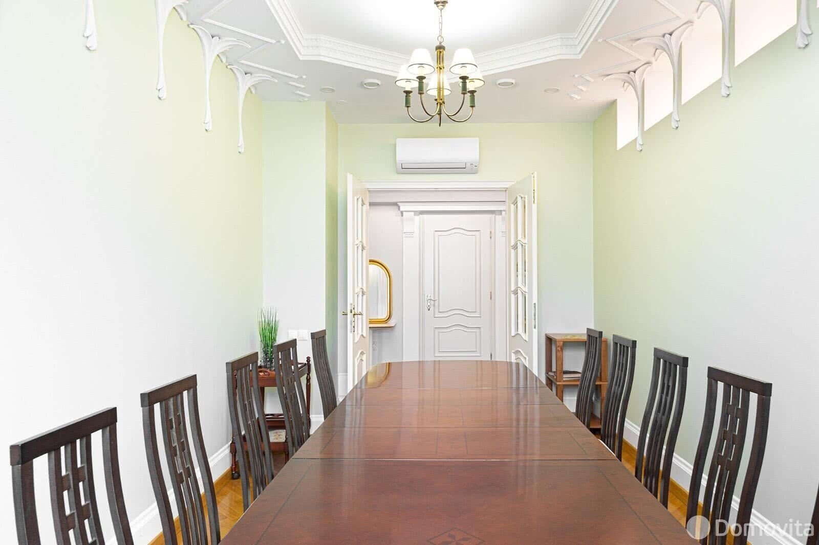 A spacious dining room with a long wooden table and chairs, a chandelier, and an air conditioning unit on the wall.