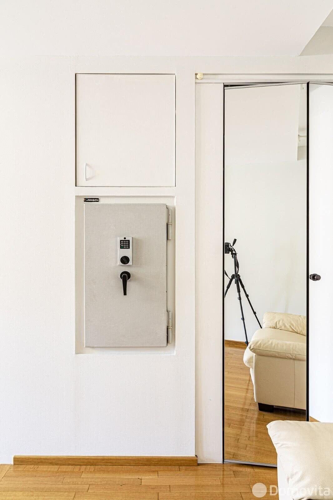 A room with a sliding door leading to a balcony, a small wall-mounted safe, and a tripod on the floor.