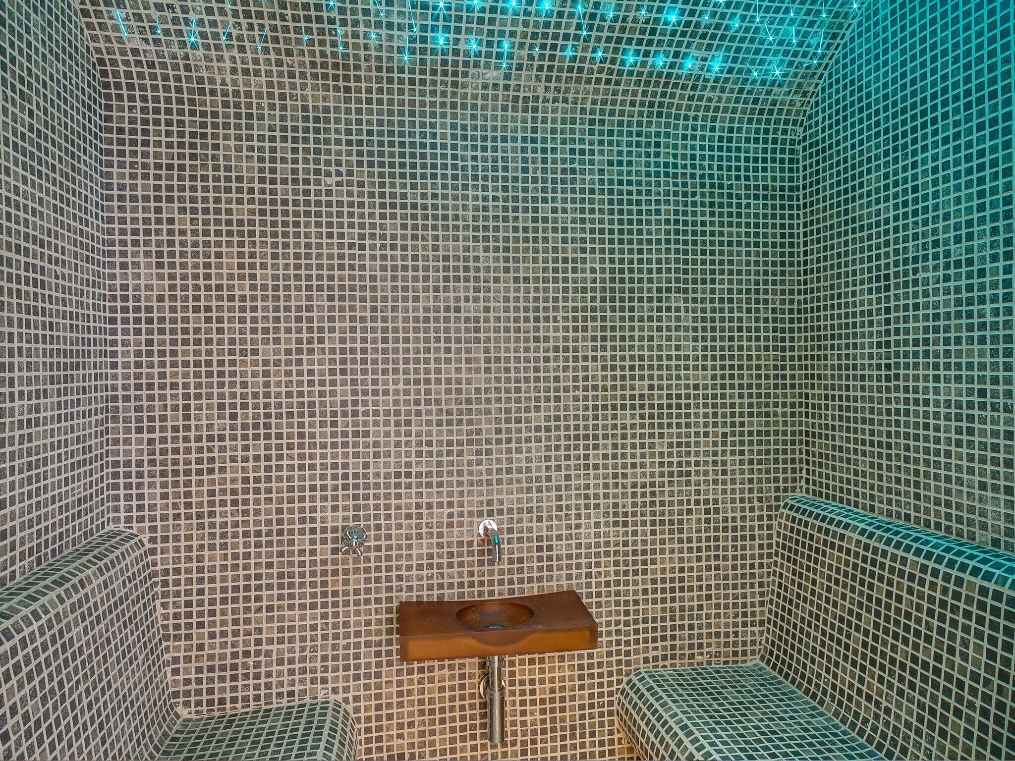 Un baño con pared de mosaicos, lavamanos de madera y un espejo pequeño.