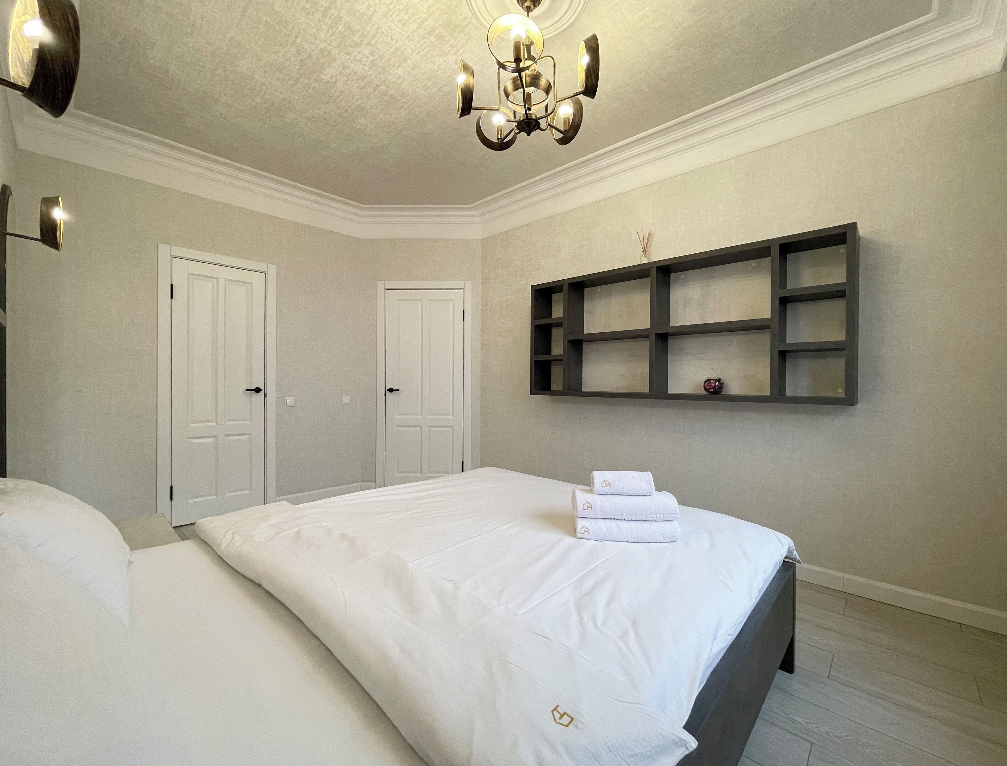 A bedroom with two beds, a chandelier, a wall-mounted shelf, and a door.