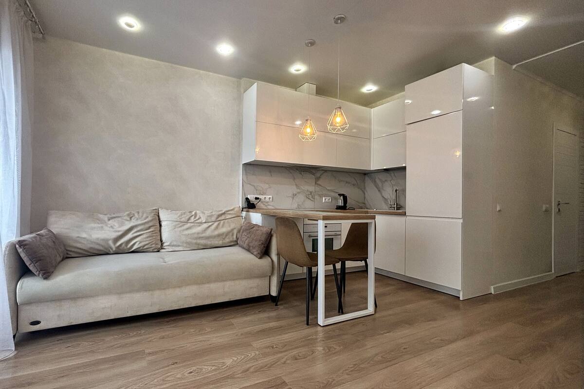 A modern kitchen with white cabinets, a marble backsplash, and a wooden dining table with two chairs.