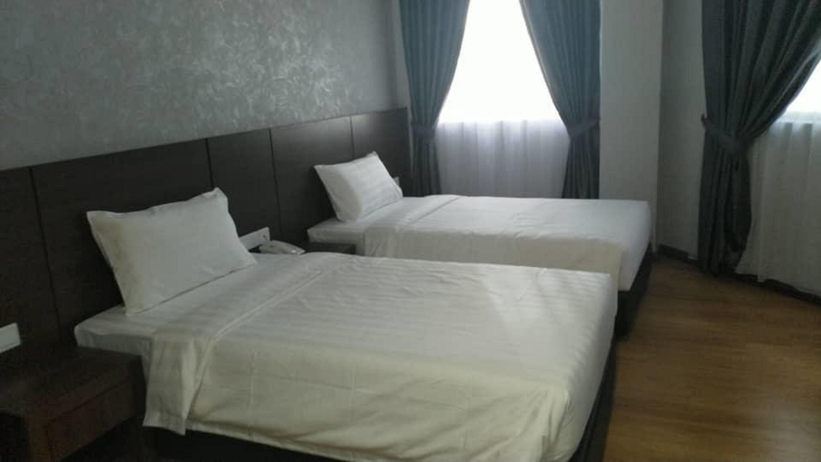 A hotel room with two beds, a wooden floor, and a large window with curtains.