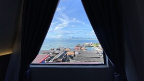 A view through a window with curtains, revealing a coastal area with buildings and a clear sky. - Grace Hotel Semporna (Semporna)