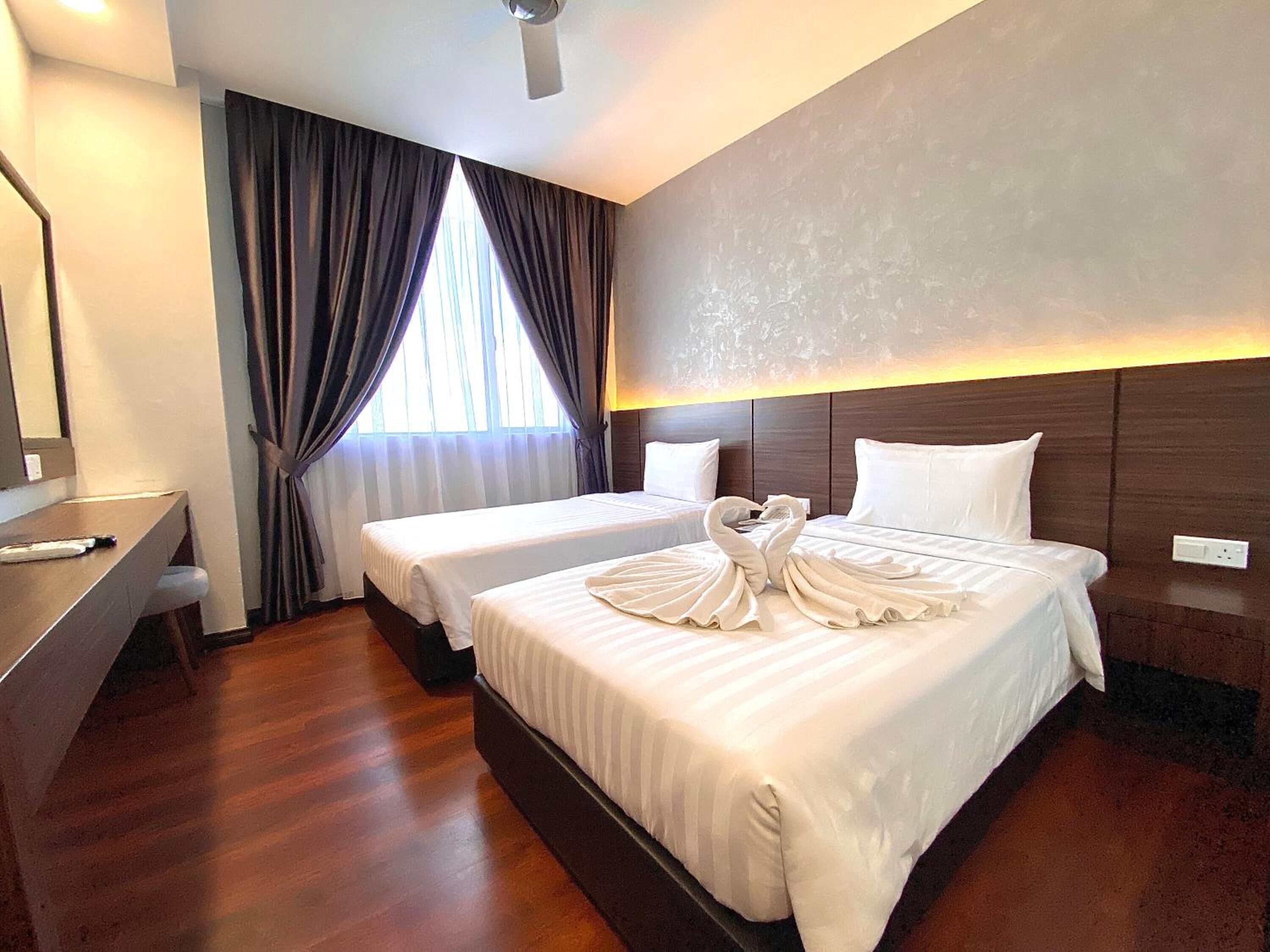 A hotel room with two beds, a desk, and a large window with curtains.