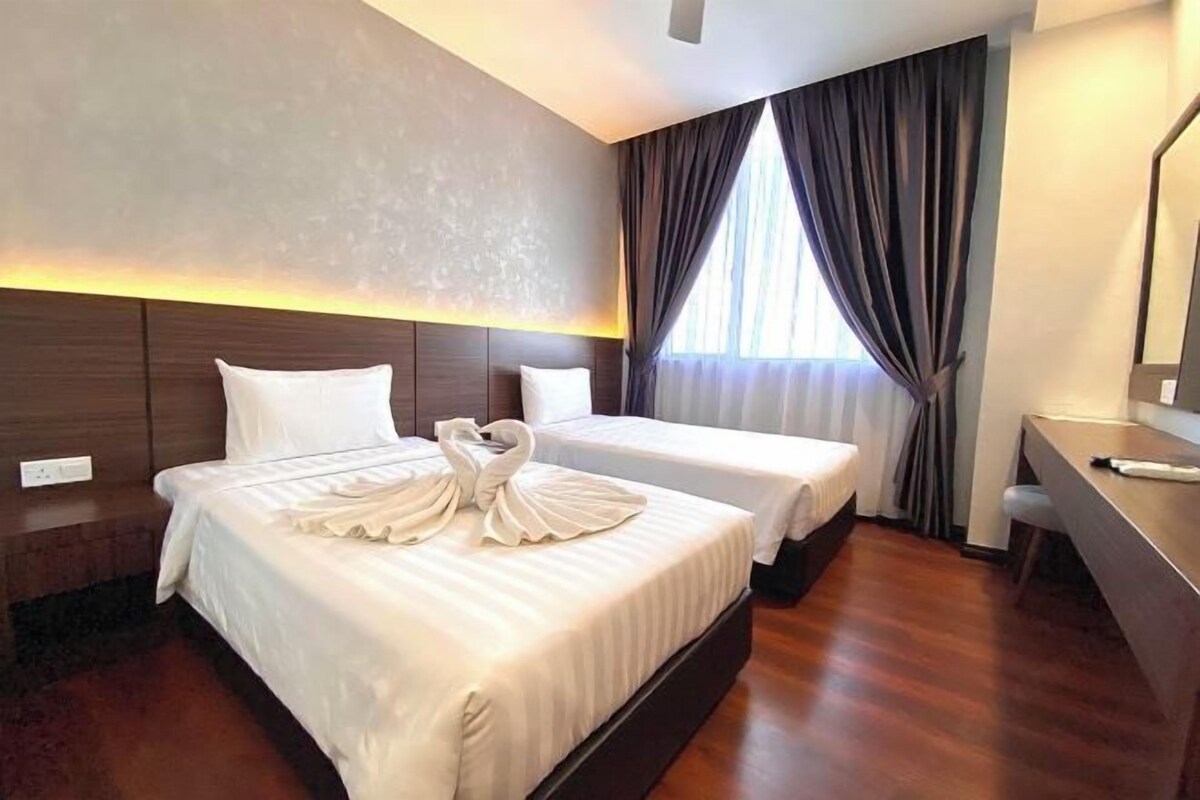 A hotel room with two beds, a desk, and a large window with curtains.