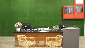 A reception desk with two computer monitors, a printer, and a red fire alarm panel on a green wall. - Grace Hotel Semporna (Semporna)