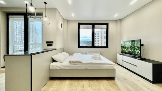 Un dormitorio moderno con cama, televisión y vista a edificios.
