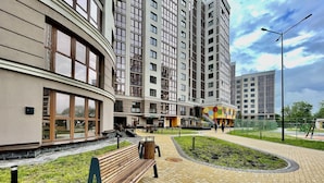 Un edificio moderno con fachada curva, ventanas amplias y un patio empedrado con un banco.
